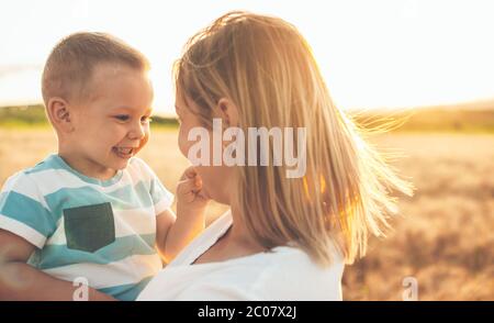 Caucasian son and his blonde mother embracing in a wheat field against the sun Stock Photo