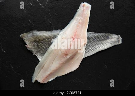 Two raw, uncooked fillets from a bass, Dicentrarchus labrax, that was caught at night beach fishing with rod and line. Displayed on a dark slate backg Stock Photo