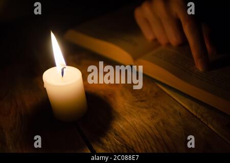 open book, a finger on a book, and a burning candle on a wooden table in the dark Stock Photo