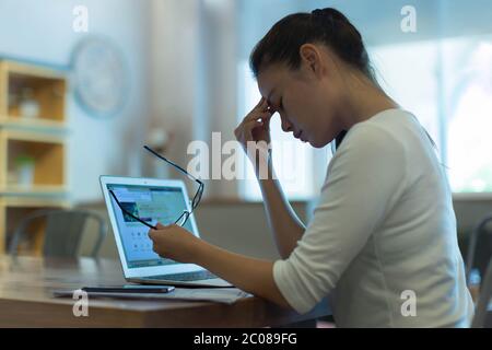 Exhausted and stressed out woman taking a break from the computer, rubbing her sore eyes. Stock Photo