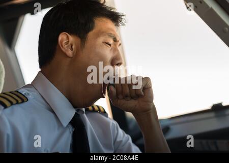 A male captain pilot sitting in the cockpit yawning while flying an airplane Stock Photo