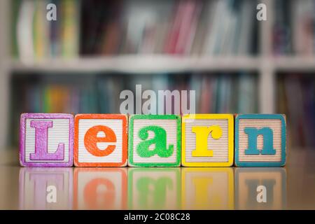 Children's toy blocks spelled the word learn with books background. School learning how to read. Stock Photo