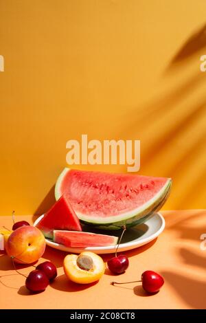 Trendy summer fruit composition with tropical leaves shadows on an orange and yellow set. Copy space Stock Photo