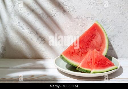 Sliced watermelon on a white rustic table and concrete wall with tropical leaves shadows. Copy space Stock Photo
