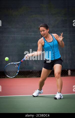 Young Japanese tennis player (model released) prepares to hit forehand stroke in competition Stock Photo