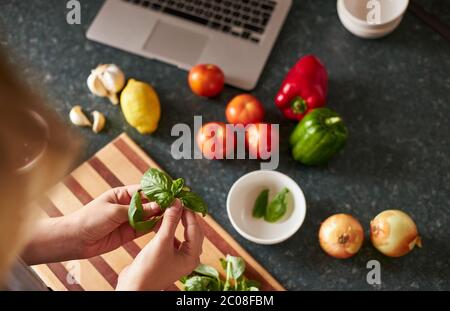 Anonymous female following online recipe preparing dinner using laptop. Stock Photo