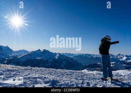 Girl enjoying sunbeams in winter with open arms at top of the mountain range. Snowboarder in late afternoon in the Swiss alps in winter. Spectacular v Stock Photo