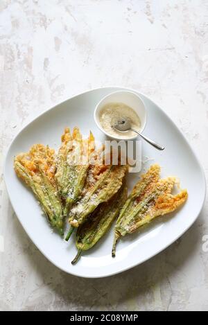 Vegetables concept. Zucchini flowers fried in batter and sprinkled with parmesan cheese on light background. Top view. Stock Photo