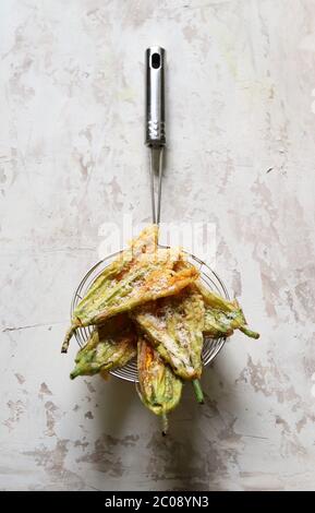 Vegetables concept. Zucchini flowers fried in batter and sprinkled with parmesan cheese on light background. Top view. Stock Photo