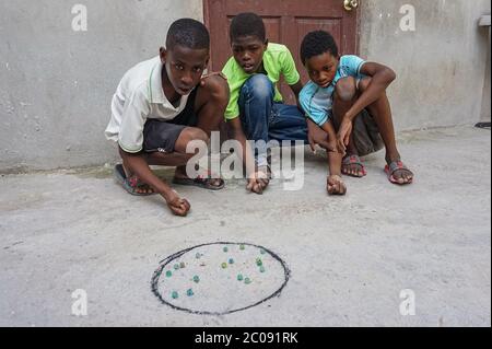 Guerby André, 14 (left to right), concentrates on his next move in a game of marbles with his school friends Gardy Mezil, 11, and Cherdnerson Jean, 13, in Port-au-Prince, Haiti. The game is popular with boys here, who often play it during school holidays. (Anne Myriam Bolivar, GPJ Haiti) Stock Photo