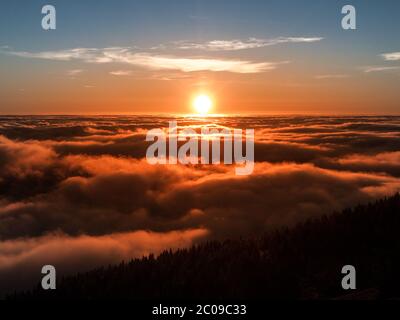 Winter sunset in the mountains. Cloudy sea is illuminated by orange rays of light.