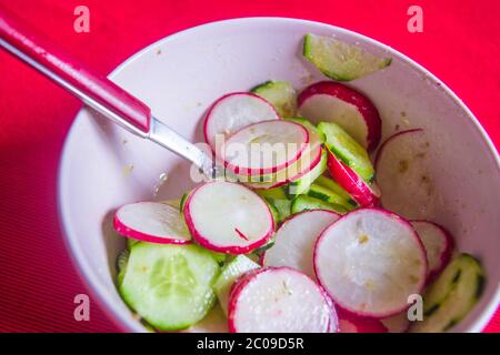 Healthy radish and courgette salad, topped with vinagraitte oil, salt, pepper, vinegar and lemon juice on scarlet red tablecloth Stock Photo