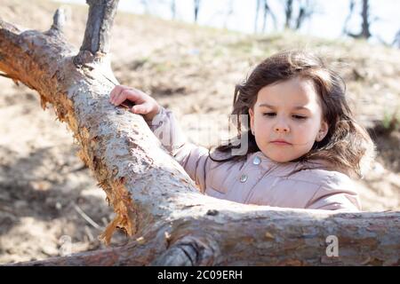 Portrait of a five year old girl standing near a tree and holding on to its trunk. Stock Photo