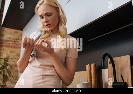 upset housewife with towel on shoulder looking at her hands in kitchen Stock Photo