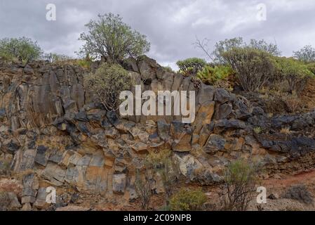 Pillow Lava or Columnar Basalt Rock forming the sides of a small Valley on the Island of Tenerife, under dark rain threatening clouds. Stock Photo