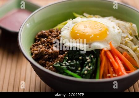 Bibimbap is a classic Korean meal. A bowl of rice is topped with seasoned vegetables, meat and a sunny side up fried egg on top. Stock Photo