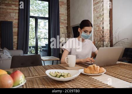 selective focus of young freelancer in medical mask using laptop Stock Photo