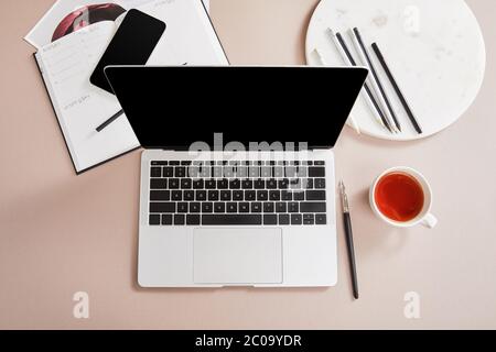 top view of cup of tea, laptop, planner, card, smartphone near circle with pencils on beige surface Stock Photo