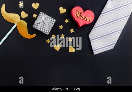 Father's day concept - gift, mustache, heart and stars on black background with the word in spanish for 'I love you'. Flat lay, top view, copy space. Stock Photo
