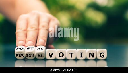 Decision for postal voting. Hand turns dice and changes the expression 'personal voting' to 'postal voting'. Stock Photo