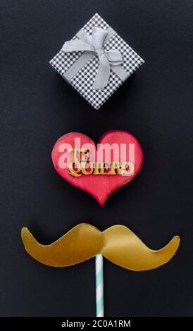 Father's day concept - gift, mustache, heart and stars on black background with the word in spanish for 'I love you'. Flat lay, top view, copy space. Stock Photo