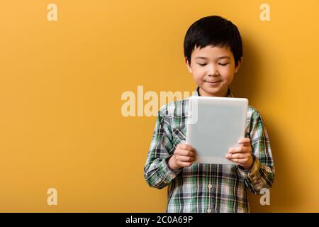 cute smiling asian boy using digital tablet on yellow Stock Photo