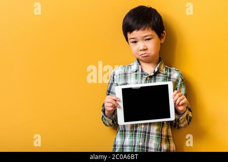 upset asian boy holding digital tablet with blank screen on yellow Stock Photo