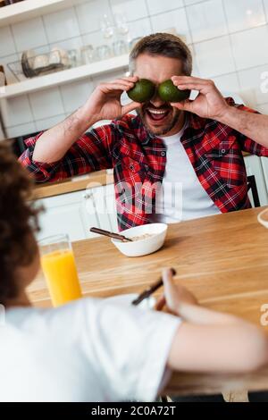 selective focus of father covering eyes with ripe avocados near curly boy Stock Photo