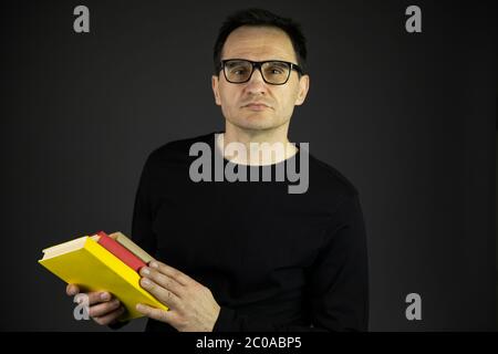 Handsome businessman in black casual clothes and glasses holding books in hands Stock Photo