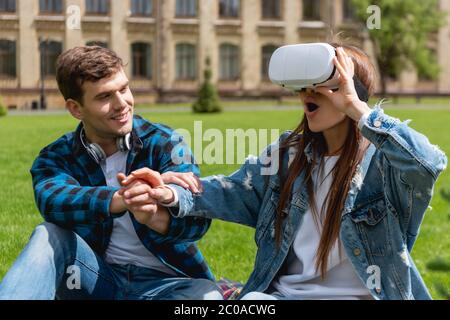 cheerful student holding hands with surprised girl in virtual reality headset Stock Photo