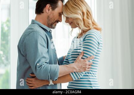 Side view of handsome man embracing smiling wife at home Stock Photo