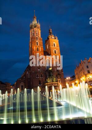 St. Mary's Church with two different towers by night (Krakow, Poland). Viewed from fountain. Stock Photo