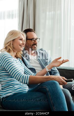 Smiling woman pointing with hand while watching tv with husband at home Stock Photo