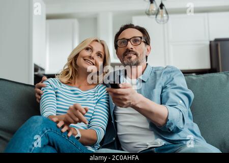 Selective focus of smiling mature couple watching tv on sofa Stock Photo
