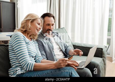 Smiling mature couple using laptop and credit card on couch Stock Photo