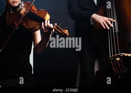 cropped view of professional musicians playing on violin and contrabass on dark stage Stock Photo