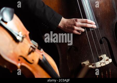 professional musician playing on double bass on dark stage with selective focus of violin Stock Photo