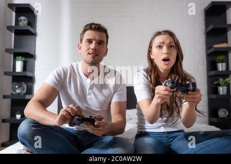 KYIV, UKRAINE - MAY 15, 2020: surprised woman and emotional man playing video game in bedroom Stock Photo