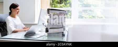 Young Businesswoman Working At Office With Stack Of Folders On Desk Stock Photo
