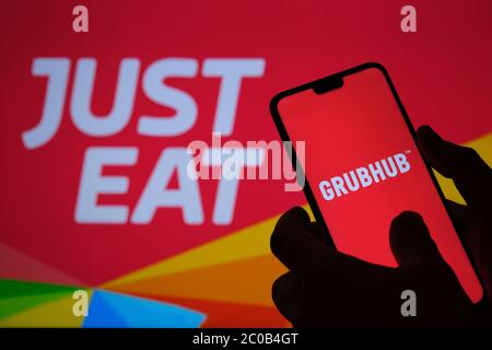 Stone / United Kingdom - June 11 2020: GRUBHUB company logo seen on smartphone silhouette and JUST EAT food delivery logo on the blurred background. C Stock Photo