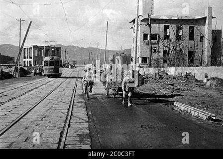 [ 1945 Japan - Atomic Bombing of Hiroshima ] — US military archival photo of the aftermath of the atomic bombing of Hiroshima, December 1945 (Showa 20).  Street view with a man pulling bedroom furniture on a cart, a cyclist and a streetcar full of people.  Warning: clear, but slightly out of focus.  20th century vintage gelatin silver print. Stock Photo