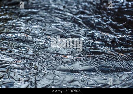 Selective focus on a fragment of the background texture of crumpled aluminum foil. Shiny wrinkled surface. Stock Photo