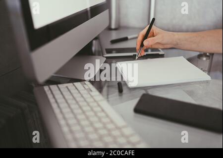 Unrecognizable woman hands writing in empty mock up notebook and computer. Freelancer using smart phone and laptop at home during quarantine. Internet Stock Photo