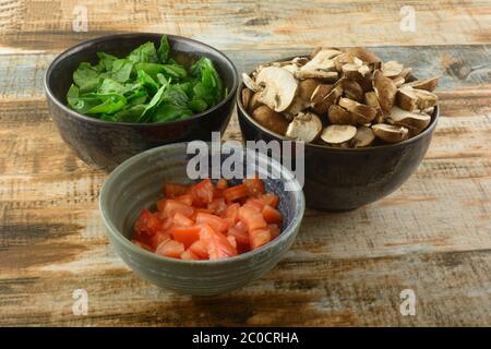 Ingredients of chopped spinach, mushrooms and tomatoes in ceramic bowls prepared for cooking Stock Photo