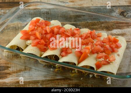 Sliced beef, mushroom ans spinach flautas or taquitos covered with crumbled queso cheese and chopped tomatoes in glass baking dish Stock Photo