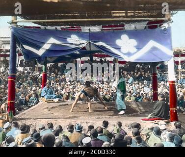 [ 1900s Japan - Japanese Sumo Wrestling ] — Sumo wrestlers in an outside arena at Eko-in Temple (回向院) in Ryogoku, Tokyo in the middle of a bout.  The temple was known as a sumo wrestling venue during the Edo (1603-1868) and Meiji (1868-1912) periods.  The first bout was held here in September 1768. From October 1833 (Tenpo 4) to 1909 (Meiji 42), the period of “Eko-in Sumo” (回向院相撲), all sumo tournaments were held at the temple.  20th century vintage glass slide. Stock Photo