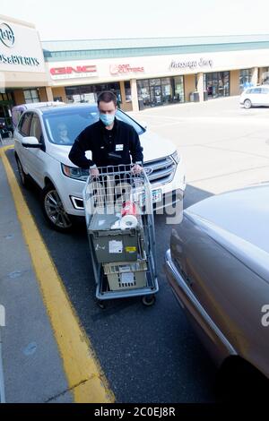 Delivery man pushing cart with groceries to load into car wearing mask & keeping socially distant at Lunds & Byerlys Store. St Paul Minnesota MN USA Stock Photo