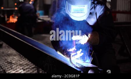 The work of the welder. Welding work on the factory floor floor. Welder in a protective mask during work. Stock Photo
