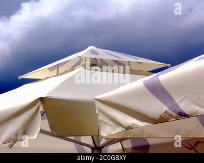 cream color canvas parasol and awning. blue and white sky on a sunny summer day. sun protection concept. UV exposure. beige and gray waterproof fabric Stock Photo