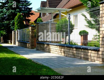 Brick fence post pier. ceramic cap stone. painted wire mesh and grille fence panels. house in the background. beautiful garden. home ownership concept Stock Photo